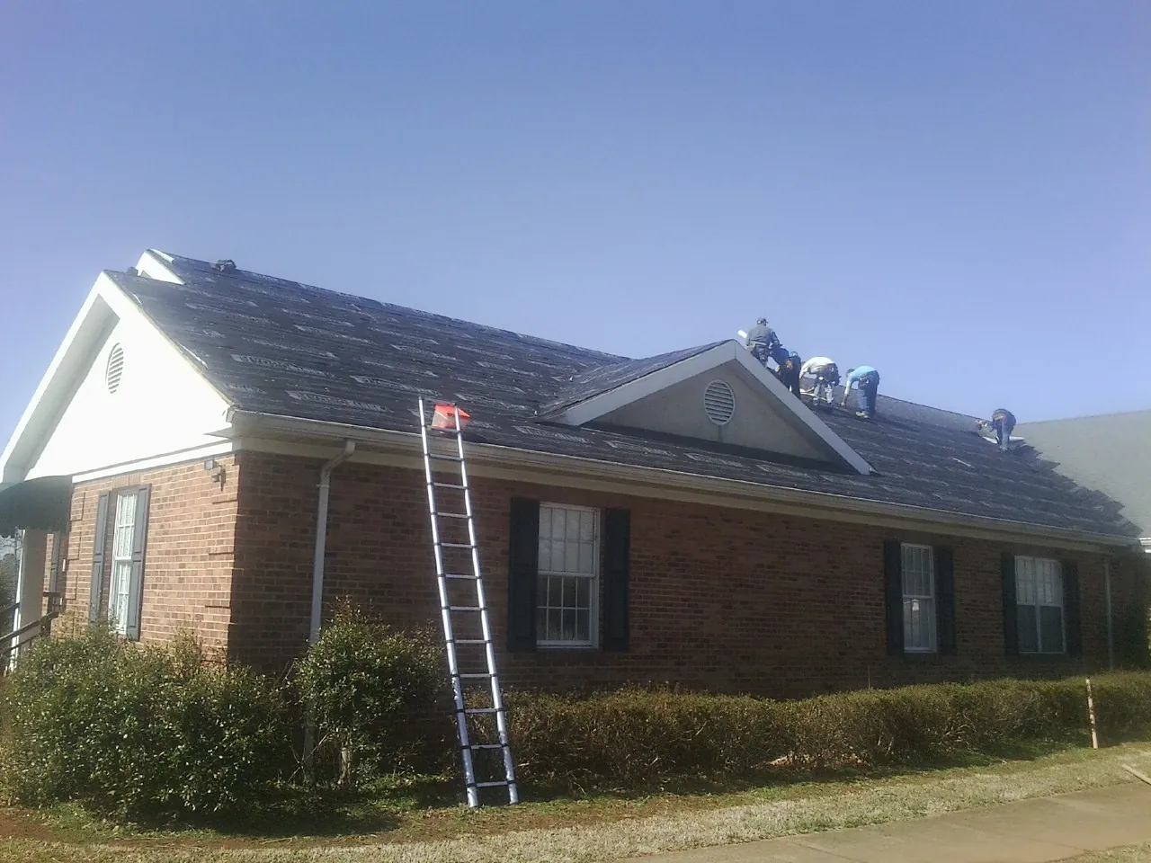 Crew tearing shingles off a brick ranch roof with a ladder set — Emergency Roof Repair work by our crew in Clear Lake