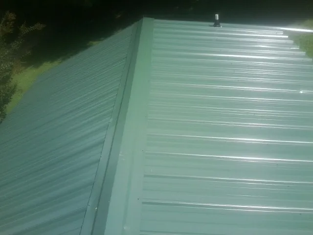 New green metal panels meeting at the ridge of a roof — Flat Roof Repair work by our crew in Clear Lake